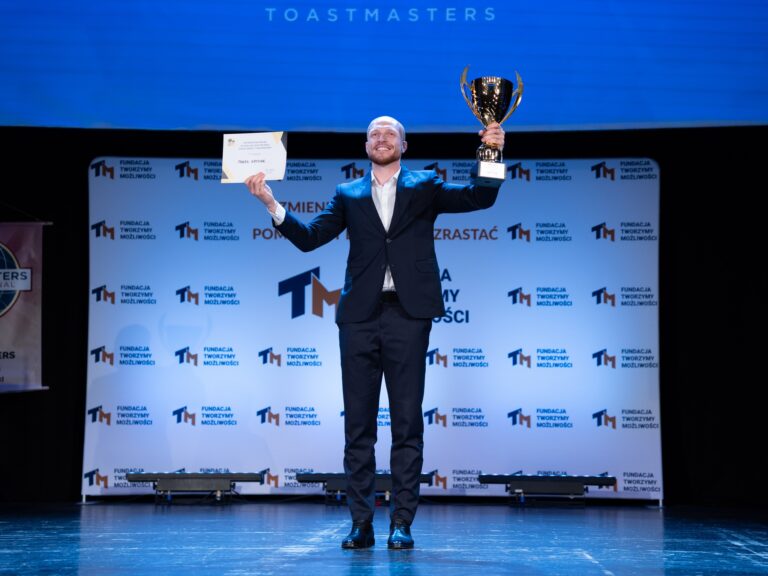 Członek klubu z pucharem i dyplomem podczas konkursu przemówień Toastmasters